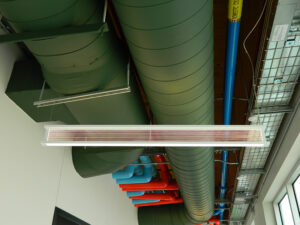 Ceiling with green ventilation ducts, red and blue pipes, and a suspended rectangular light fixture.