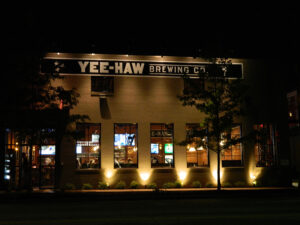 Exterior of Yee-Haw Brewing Co. at night, with illuminated windows and a lit sign on the building front.