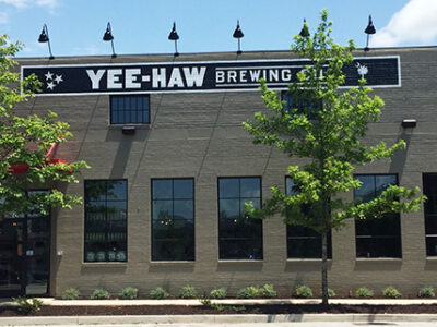 Front view of Yee-Haw Brewing Co. building with large windows and trees along the sidewalk.