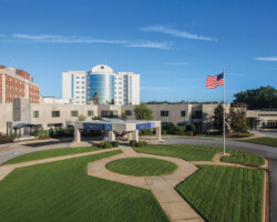 Healthcare Projects Exterior view of a hospital building complex with a circular driveway and an American flag on a pole in the foreground.