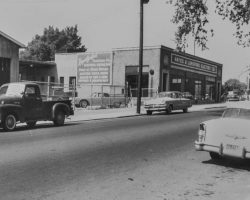 Vintage street scene with classic cars parked near "Hayes & Lunsford Electric Co." building and an Esso sign, circa mid-20th century.